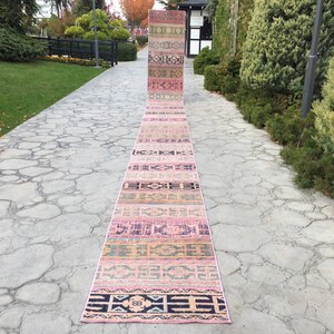 Può includere: Un tappeto lungo e stretto con motivi geometrici rosa e neri. Il tappeto è steso su un vialetto di pietra.