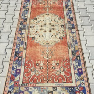 May include: A vintage Turkish runner rug with a red background and a central medallion design. The rug has a blue, white, and orange border with floral and geometric patterns.