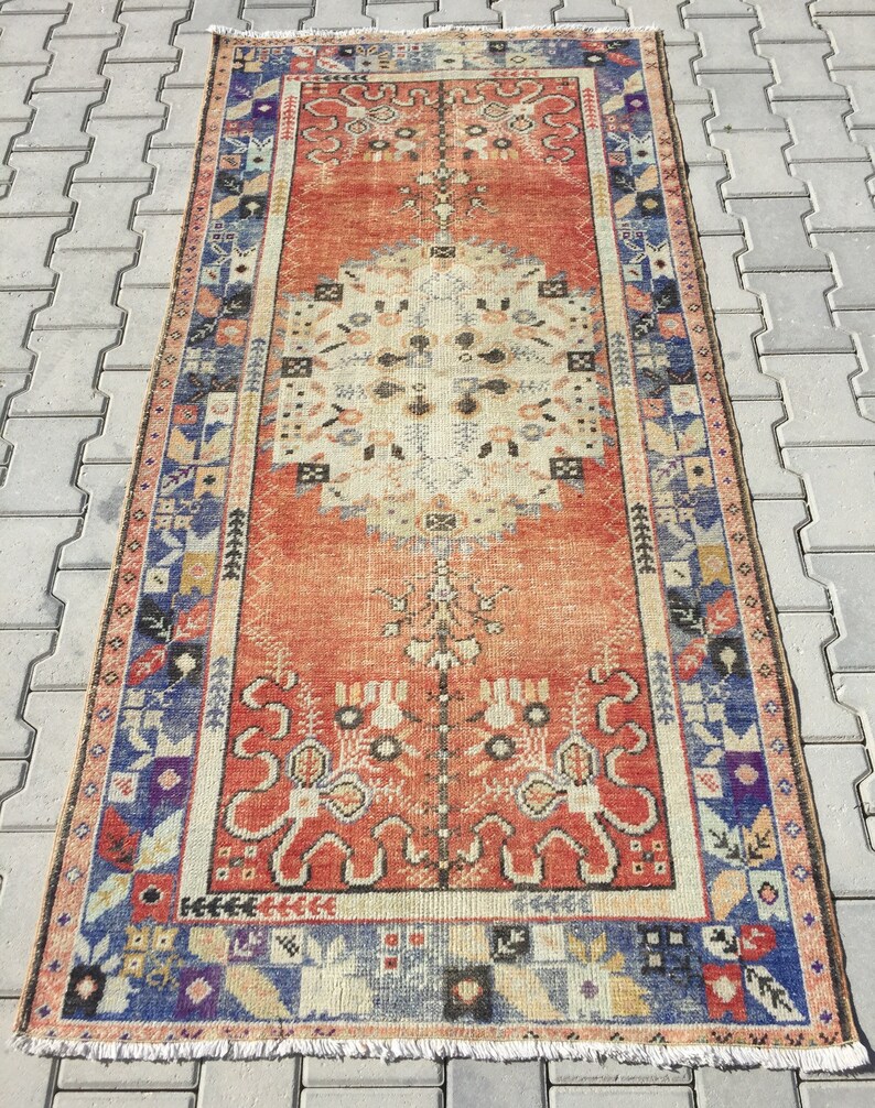 May include: A vintage Turkish runner rug with a red background and a central medallion design. The rug has a blue, white, and orange border with floral and geometric patterns.