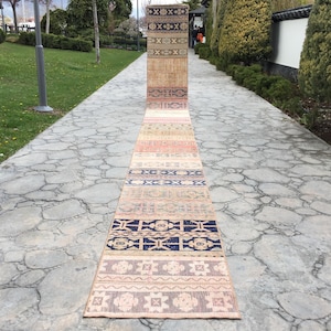 May include: A long, narrow rug with a colorful geometric pattern. The rug is made of woven fabric and has a fringe on each end. The rug is laid out on a stone path.
