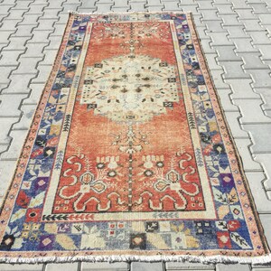 May include: A vintage rug with a red background and a central medallion in shades of beige and cream. The rug has a blue and beige border with intricate floral and geometric patterns.
