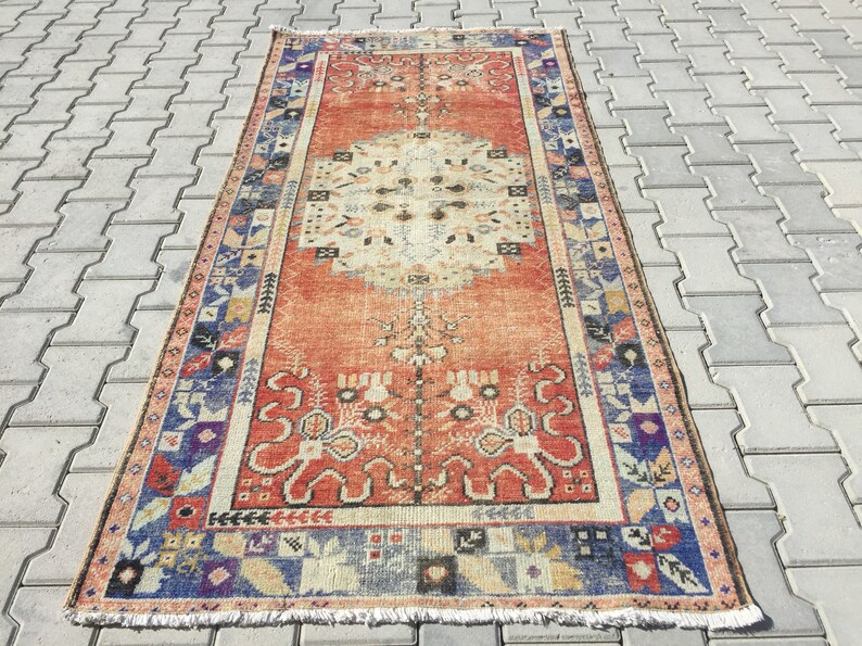 May include: A vintage rug with a red background and a central medallion in shades of beige and cream. The rug has a blue and beige border with intricate floral and geometric patterns.