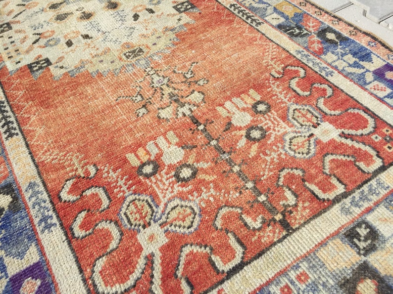 May include: A vintage rug with a red, cream, and blue geometric pattern. The rug has a worn, distressed look and features a central floral design.