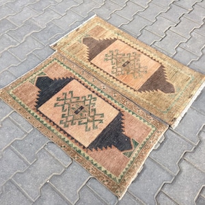 May include: Two small, rectangular rugs with a geometric pattern in shades of brown, green, and beige. The rugs have a fringed border.