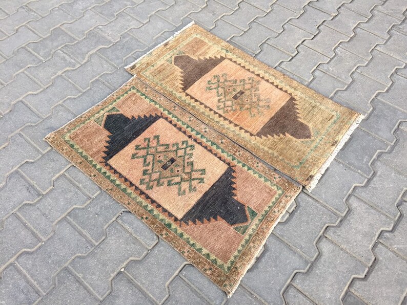 May include: Two small, rectangular rugs with a geometric pattern in shades of brown, green, and beige. The rugs have a fringed border.