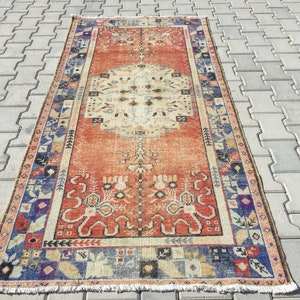 May include: A vintage rug with a red, orange, and cream color scheme. The rug has a geometric pattern with a central medallion and a border of floral motifs.