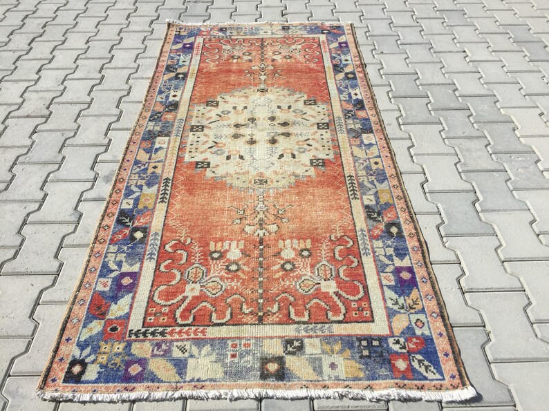 May include: A vintage rug with a red, orange, and cream color scheme. The rug has a geometric pattern with a central medallion and a border of floral motifs.