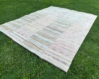 May include: A large, rectangular, handwoven rug with a patchwork design. The rug is made of natural fibers and has a light blue, brown, and beige color scheme. The rug has a striped pattern with geometric designs.