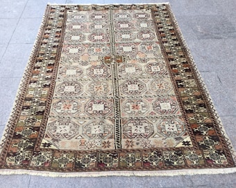 May include: A traditional Turkish rug with a beige background and intricate geometric patterns in shades of brown, red, and green. The rug has a fringe border.