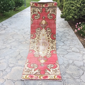Könnte beinhalten: Ein rosafarbener und cremefarbener Vintage-Teppich mit einem floralen Muster. Der Teppich ist aufgerollt und liegt auf einem Steinweg.