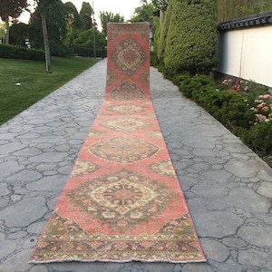 May include: A long, narrow, pink and cream colored rug with a floral pattern. The rug is laid out on a stone walkway.