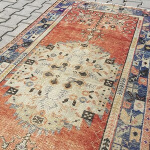 May include: A vintage rug with a faded orange, cream, and blue color scheme. The rug has a traditional Persian design with intricate floral patterns and geometric shapes.