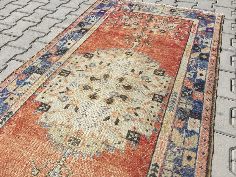 May include: A vintage rug with a faded orange, cream, and blue color scheme. The rug has a traditional Persian design with intricate floral patterns and geometric shapes.