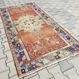 May include: A vintage Turkish rug with a red, white, and blue color scheme. The rug has a floral pattern and a fringed edge.