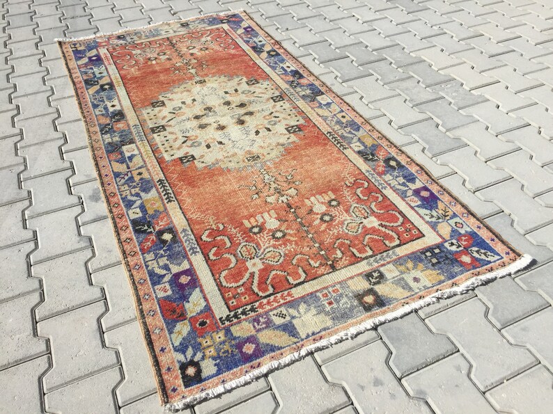 May include: A vintage Turkish rug with a red, white, and blue color scheme. The rug has a floral pattern and a fringed edge.