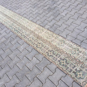 May include: A long, narrow runner rug with a traditional Persian design. The rug has a cream background with green and brown floral patterns.