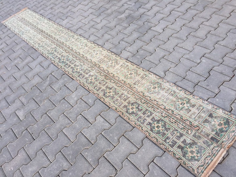 May include: A long, narrow runner rug with a traditional Persian design. The rug has a cream background with green and brown floral patterns.