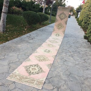 May include: A long, pink and cream runner rug with a geometric pattern. The rug is laid out on a gray concrete walkway.
