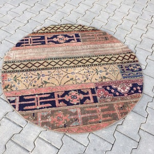 Może przedstawiać: Okrągły, wielokolorowy dywan patchworkowy z różnymi wzorami geometrycznymi i kwiatowymi. Dywan jest wykonany z wełny i ma zużyty, vintage'owy wygląd.