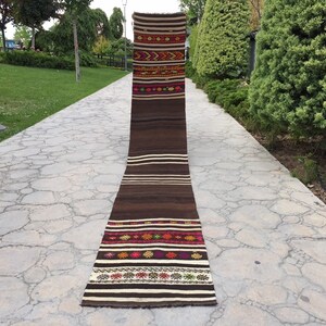 Puede incluir: Una alfombra larga y estrecha de color marr&oacute;n y blanco con patrones geom&eacute;tricos coloridos tejidos en el dise&ntilde;o. La alfombra est&aacute; colocada en un camino de piedra.