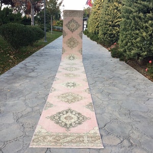 May include: A pink and cream runner rug with a traditional floral pattern. The rug is laid out on a gray concrete walkway.