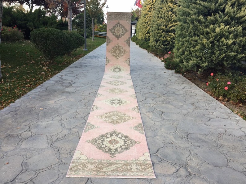 May include: A pink and cream runner rug with a traditional floral pattern. The rug is laid out on a gray concrete walkway.