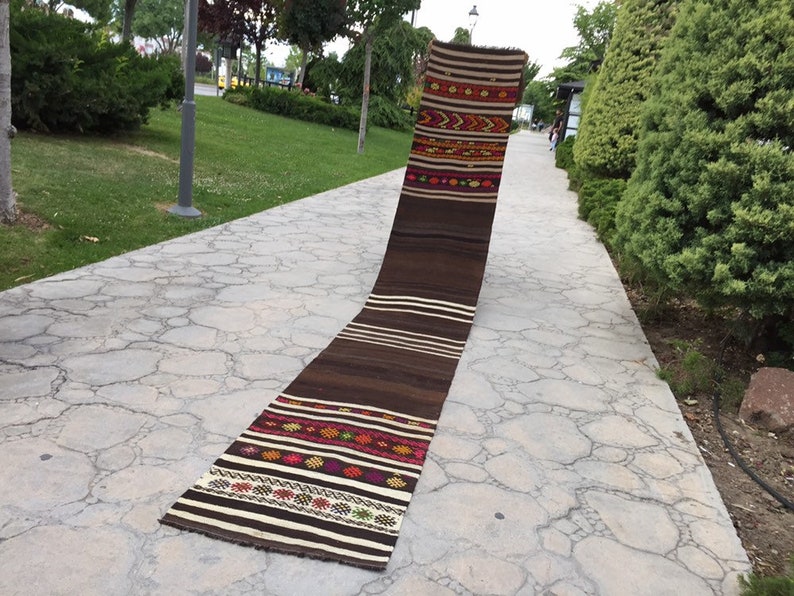 Puede incluir: Una alfombra larga, marr&oacute;n y blanca tejida con patrones geom&eacute;tricos coloridos. La alfombra est&aacute; colocada en un camino de piedra.