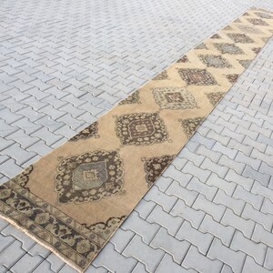 Pu&ograve; includere: Un tappeto da corridoio lungo e beige con un motivo geometrico in tonalit&agrave; di marrone, beige e blu. Il tappeto ha un bordo con frange.