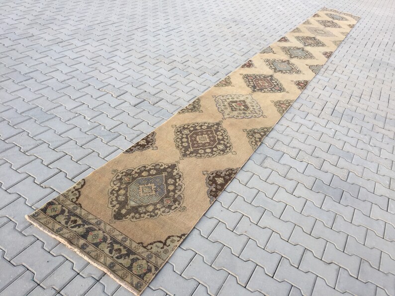 Pu&ograve; includere: Un tappeto da corridoio lungo e beige con un motivo geometrico in tonalit&agrave; di marrone, beige e blu. Il tappeto ha un bordo con frange.