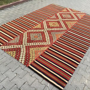 Peut inclure: Un tapis kilim turc vintage avec un motif géométrique dans des tons de rouge, orange, jaune, bleu et noir. Le tapis a une bordure rayée et un motif central en losange.