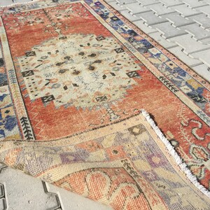 May include: A vintage, hand-woven rug with a red, cream, and blue geometric pattern. The rug has a fringe border and is folded in half.