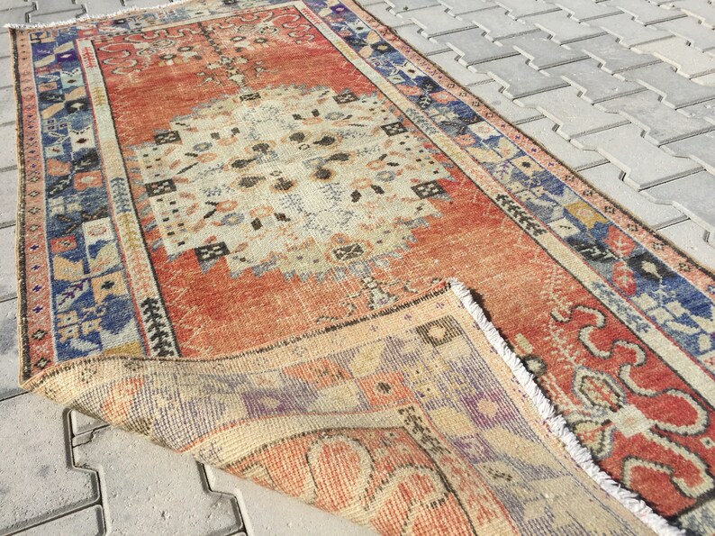 May include: A vintage, hand-woven rug with a red, cream, and blue geometric pattern. The rug has a fringe border and is folded in half.
