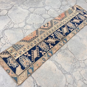 Op de afbeelding: Een lang, smal tapijt met een traditioneel Turks ontwerp. Het tapijt is voornamelijk beige met blauwe en oranje accenten. Het patroon bevat geometrische vormen en gestileerde bloemmotieven.