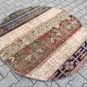 May include: Round patchwork rug with a variety of patterned stripes in shades of beige, red, blue, and brown. The rug has a vintage, distressed appearance, with visible wear and tear adding to its character. The rug is placed on a gray brick surface.