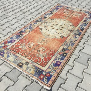 May include: A vintage rug with a faded orange background and a central medallion in a lighter shade. The rug has a blue, red, and white border with intricate floral and geometric patterns.