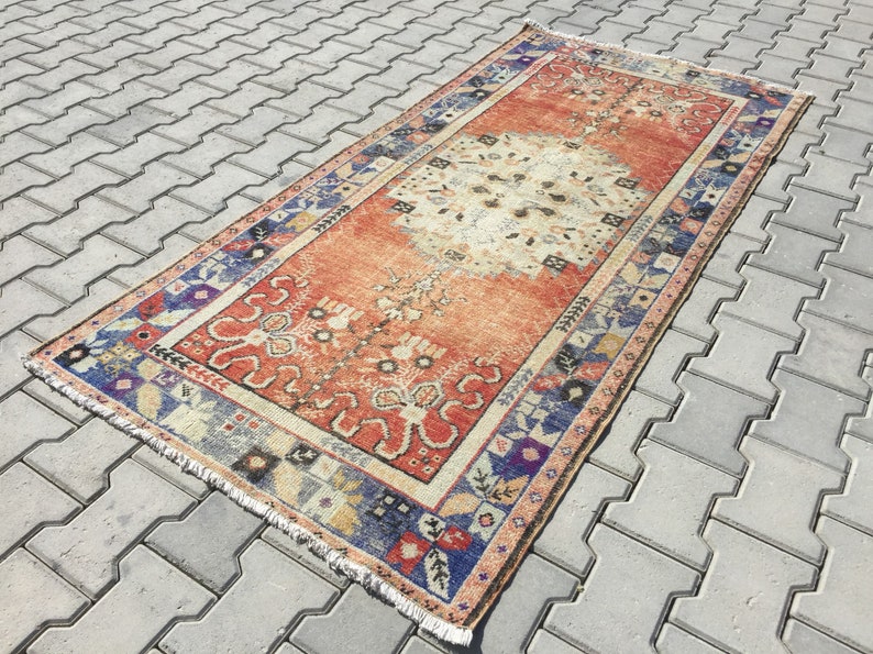 May include: A vintage rug with a faded orange background and a central medallion in a lighter shade. The rug has a blue, red, and white border with intricate floral and geometric patterns.