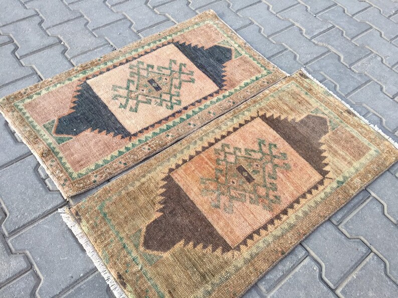 May include: Two small, rectangular rugs with a geometric pattern in shades of brown, green, and pink. The rugs have a fringed border.