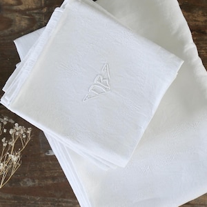 May include: A stack of white linen napkins with embroidered details. The napkins are folded and arranged on a wooden surface.