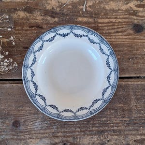 Könnte beinhalten: Eine weiße Keramikschale mit blauem Blumenmuster am Rand. Die Schale hat einen gewellten Rand und eine tiefe Mitte. Das blaue Muster ist detailliert und dekorativ, vor weißem Hintergrund. Die Schale ist wahrscheinlich Vintage oder antik.