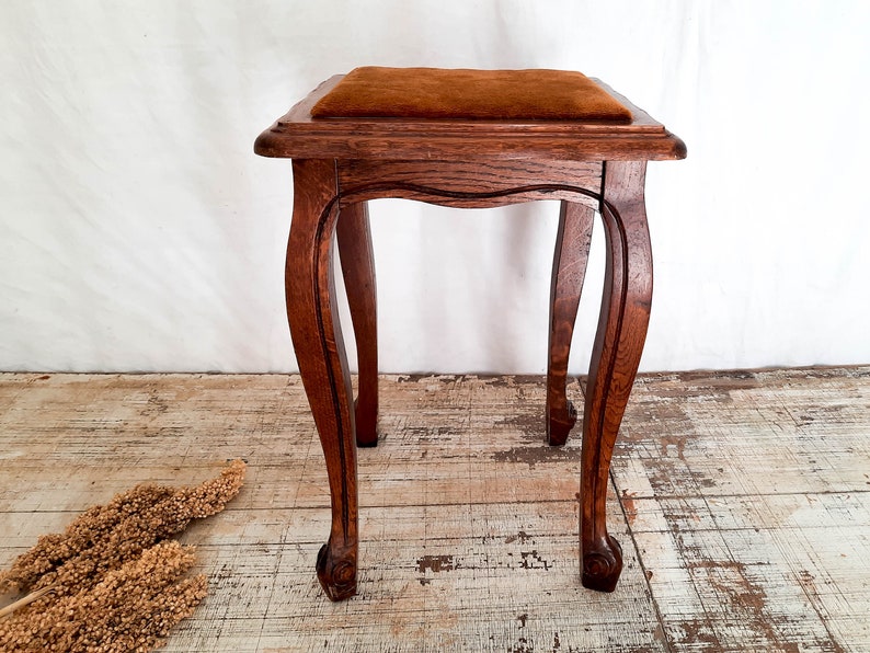 Peut inclure: Petit tabouret en bois de couleur marron fonc&eacute; avec un coussin marron. Les pieds sont incurv&eacute;s et sculpt&eacute;s. Le tabouret est de style ancien. Dimensions: environ 40 cm de hauteur, 30 cm de largeur et de profondeur.