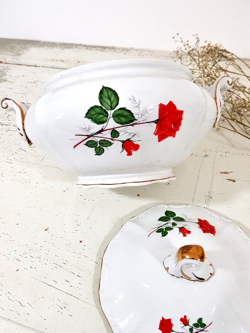 May include: White porcelain serving bowl with a lid. The bowl and lid feature a red rose with green leaves and gold trim.