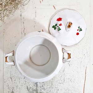 May include: White porcelain serving bowl with a lid. The lid has a gold trim and a floral design with red roses. The bowl has two gold handles.
