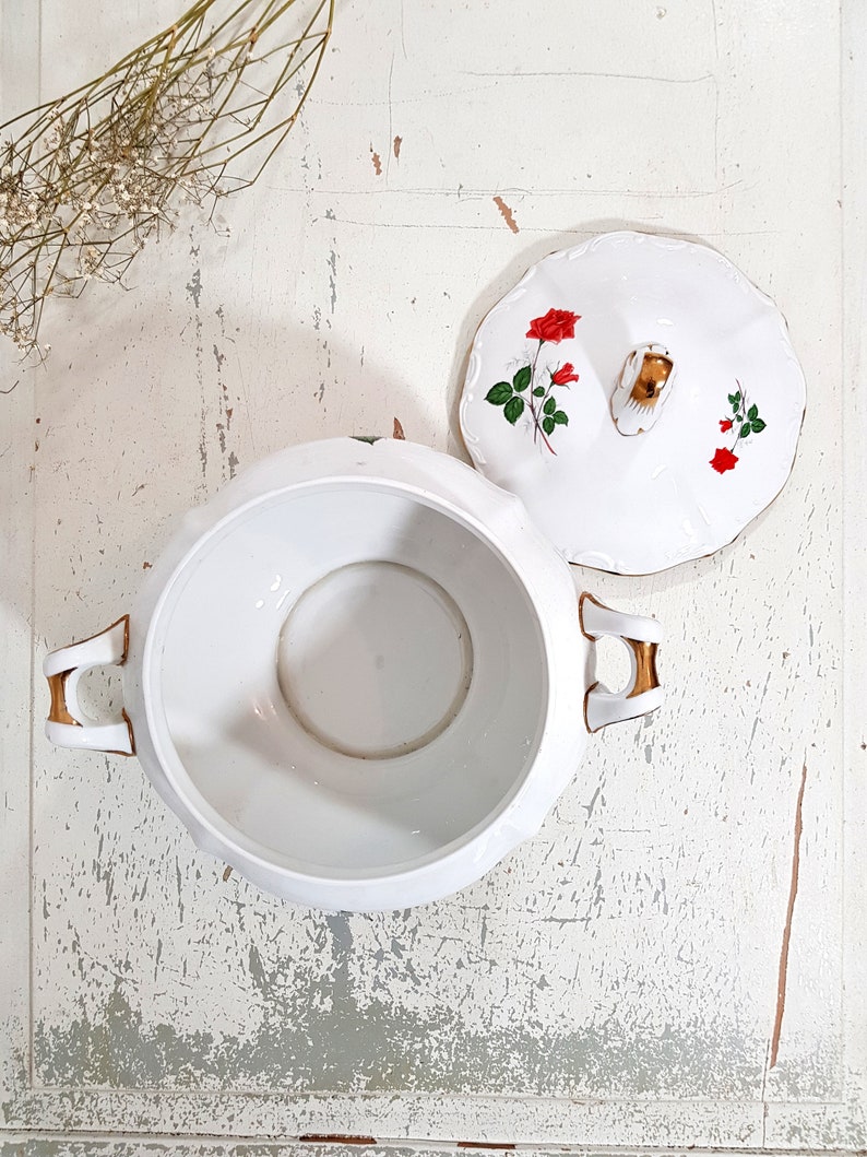 May include: White porcelain serving bowl with a lid. The lid has a gold trim and a floral design with red roses. The bowl has two gold handles.