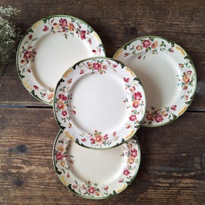 Puede incluir: Juego de cuatro platos de cena vintage con estampado floral, fondo blanco, borde verde y dorado y diseños florales rojos y amarillos.