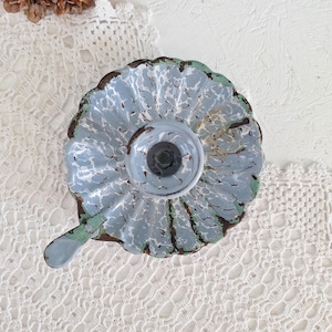 May include: A light blue and white speckled enamel candle holder with a scalloped edge, a central circular candle cup, and a small handle extending from the side. The metal surface shows visible brown rust along the edges and ridges.