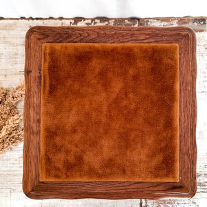 Peut inclure: Un plateau carr&eacute; en bois avec une finition marron fonc&eacute;. Il pr&eacute;sente un insert en velours orange-brun. Le plateau est pos&eacute; sur une surface en bois blanchi rustique, avec des plantes s&eacute;ch&eacute;es dans le coin.