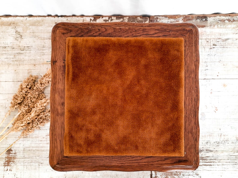 Peut inclure: Un plateau carr&eacute; en bois avec une finition marron fonc&eacute;. Il pr&eacute;sente un insert en velours orange-brun. Le plateau est pos&eacute; sur une surface en bois blanchi rustique, avec des plantes s&eacute;ch&eacute;es dans le coin.