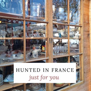 Peut inclure: Une vitrine en bois remplie de divers objets anciens en verre et en porcelaine. Le texte "HUNTED IN FRANCE just for you" est affich&eacute; sur un rectangle blanc. La fen&ecirc;tre refl&egrave;te l'environnement ext&eacute;rieur.
