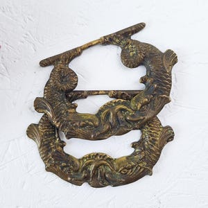 May include: Antique bronze-colored metal decorative hardware featuring a fish design. The hardware has a detailed, textured surface and is likely for furniture or a similar application. The design includes two fish and a decorative bar.