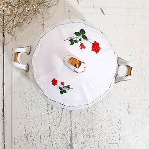 May include: White porcelain serving dish with a gold trim and a floral design featuring red roses and green leaves.